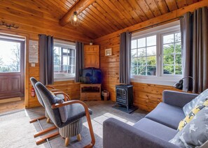 A cozy cabin interior with a wooden interior, a sofa, a rocking chair, a television, and a fireplace.
