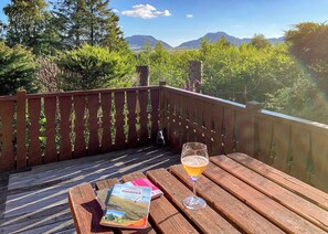 Une terrasse en bois, une bière à la main et un livre, le tout entouré de verdure et de montagnes.