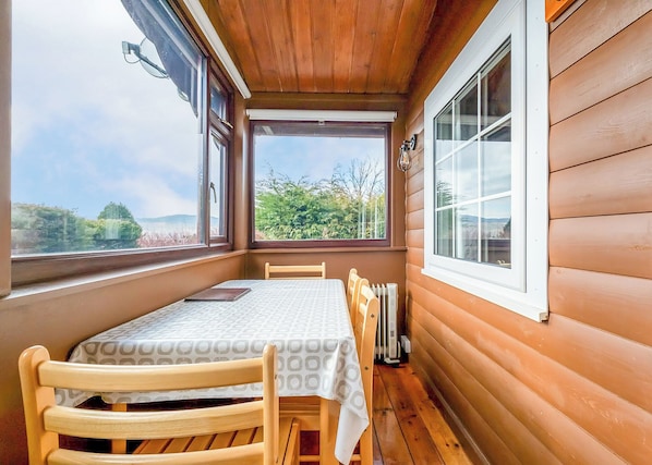 A wooden cabin with a table and chairs, large windows, and a view of the outdoors.