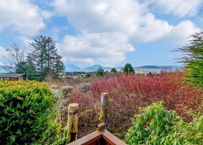 Un paysage rural avec une clôture en bois, une végétation luxuriante et des montagnes lointaines sous un ciel partiellement nuageux.
