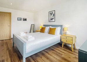 A neatly made bed with towels, a bedside table with a lamp, a wooden door, and a framed picture on the wall. - 1 bedroom accommodation in Old Buckenham (Old Buckenham)
