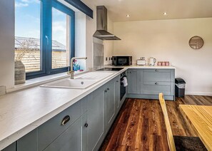 A modern kitchen with a large window, stainless steel appliances, and grey cabinetry. - 2 bedroom accommodation in Old Buckenham (Old Buckenham)