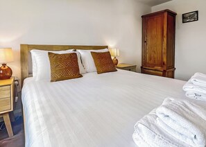 A hotel room with a large bed, two bedside lamps, a wooden wardrobe, and neatly folded towels. - 2 bedroom accommodation in Old Buckenham (Old Buckenham)