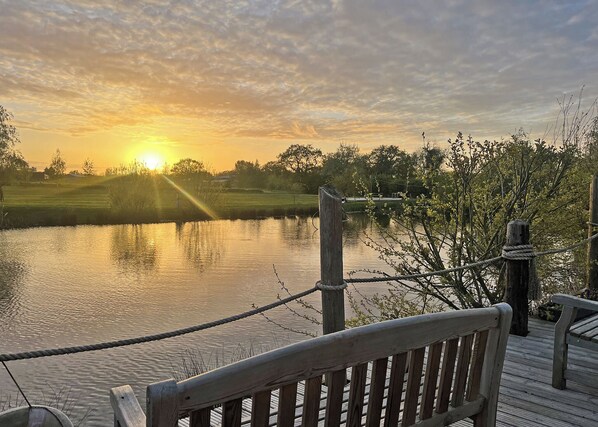 A wooden deck overlooking a calm body of water with a sunset in the background.