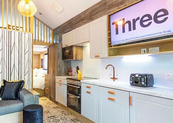 A modern kitchen with white cabinets, a built-in oven, a microwave, and a large screen displaying 'Three'.