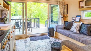 Ein gemütlicher Raum mit einer Couch, einem Esstisch und Stühlen, einer Küchenzeile und einer großen Schiebeglastür, die auf eine Terrasse im Freien führt.