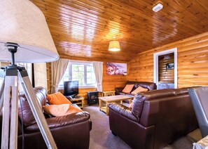 Interior de una cabaña de madera con sofá, televisor y lámpara.