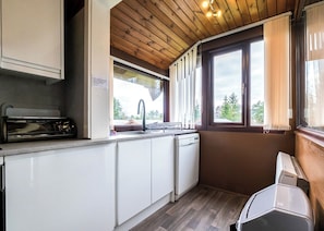 Una cocina compacta con armarios blancos, lavavajillas integrado, un lavabo con grifo y una ventana con cortinas.