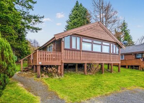 A wooden cabin with a deck, large windows, and a satellite dish.