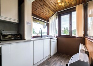Eine kleine Küche mit weißen Schränken, einem eingebauten Geschirrspüler, einem Spülbecken mit Armatur und einem Fenster mit Vorhängen.