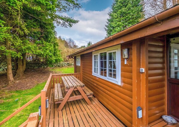 A wooden cabin with a deck, a window, and a door.