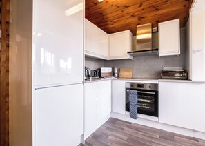 Una cocina moderna con armarios blancos, horno de acero inoxidable y techo de madera.