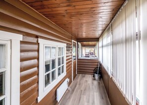 A log cabin interior with a wooden floor, white-framed windows, and a view to the outside.