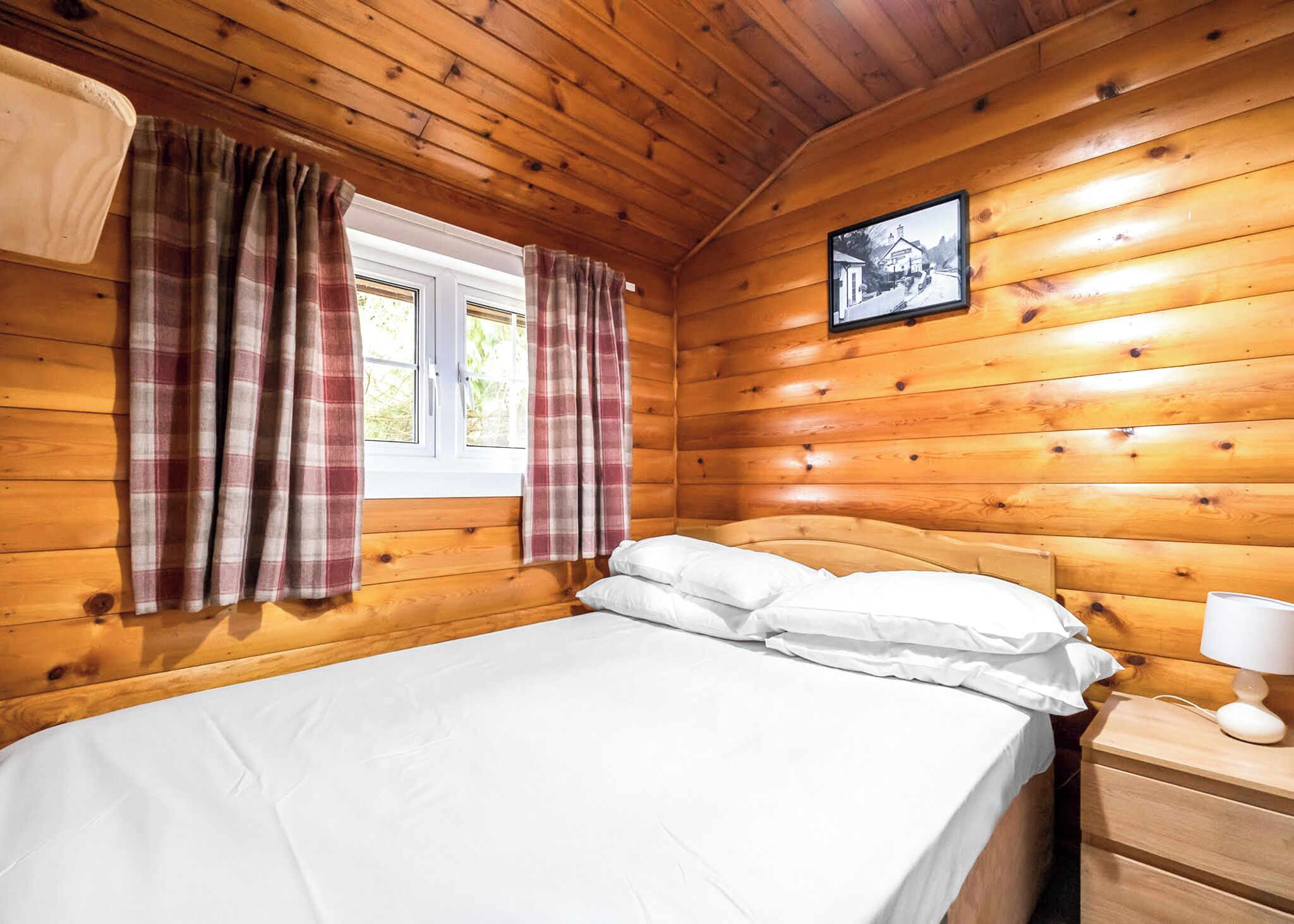 Une pièce de style cabane en bois, avec un lit, des rideaux, une table de chevet et un tableau encadré au mur.