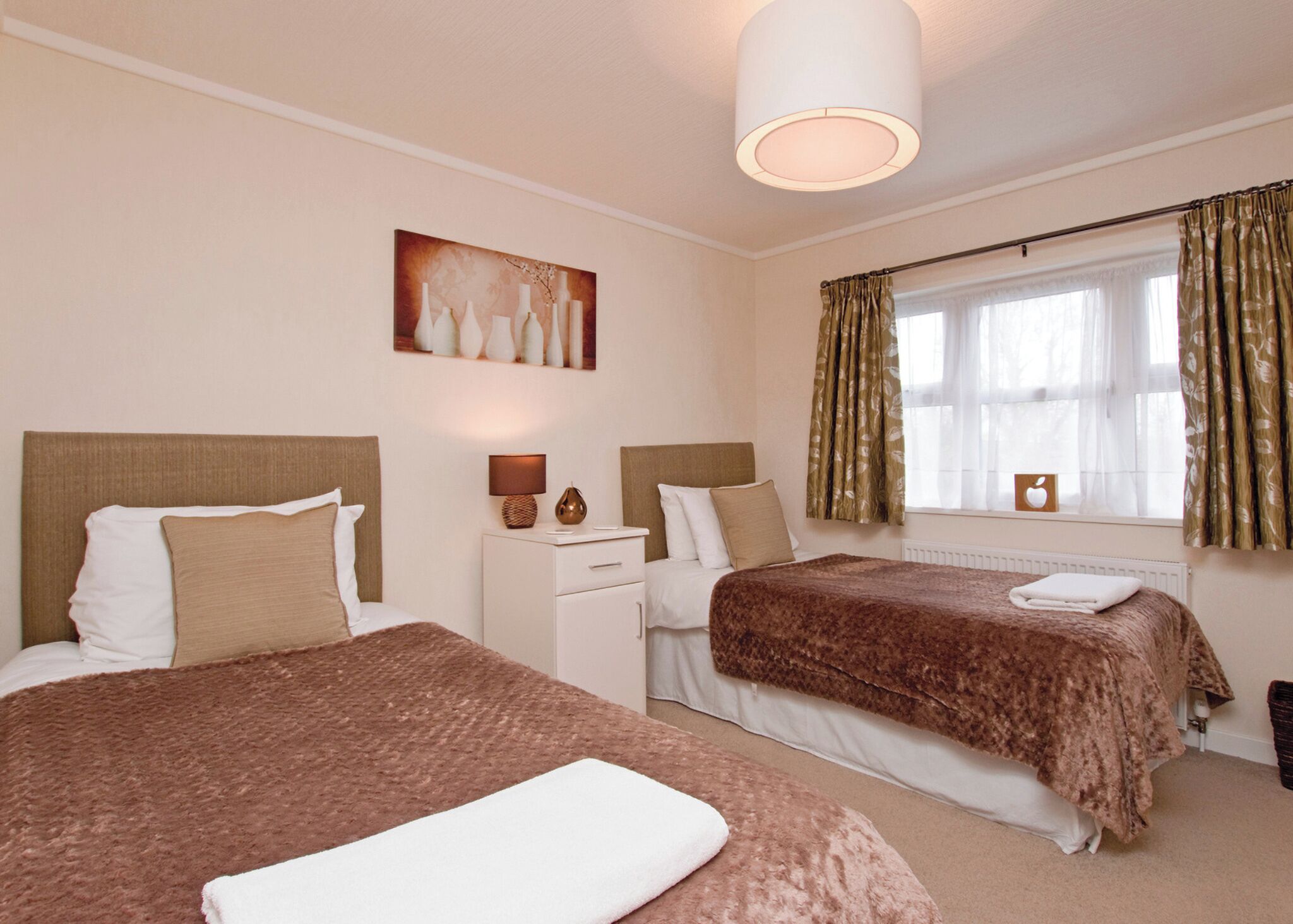A hotel room with two beds, a nightstand, a lamp, a painting, and a window with curtains.