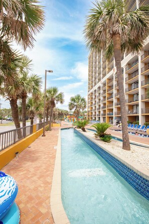A pool area with palm trees, a tiled pool, and a building with balconies. - Beachview Bliss, KING Bed, Pools, Lazy River, Hot Tubs, No Resort Fees, M23 (Myrtle Beach)