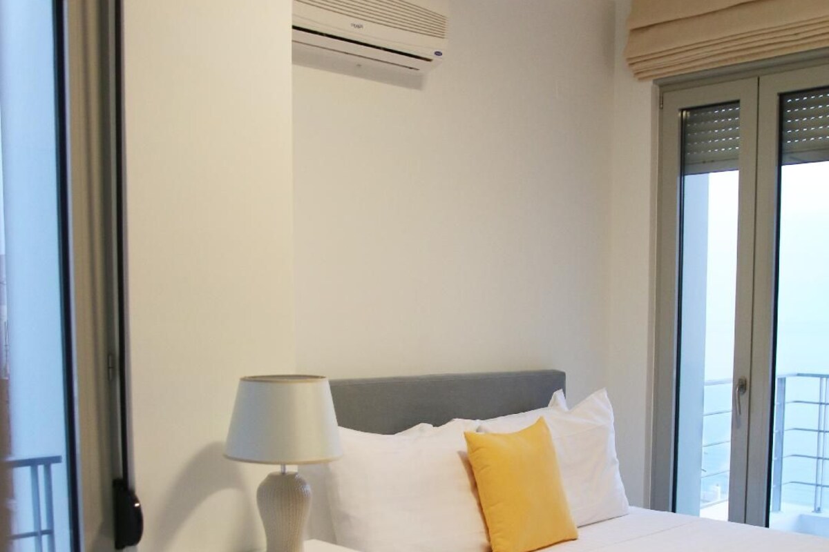 A hotel room with a bed, a nightstand with a lamp, a window with a view, and an air conditioning unit.