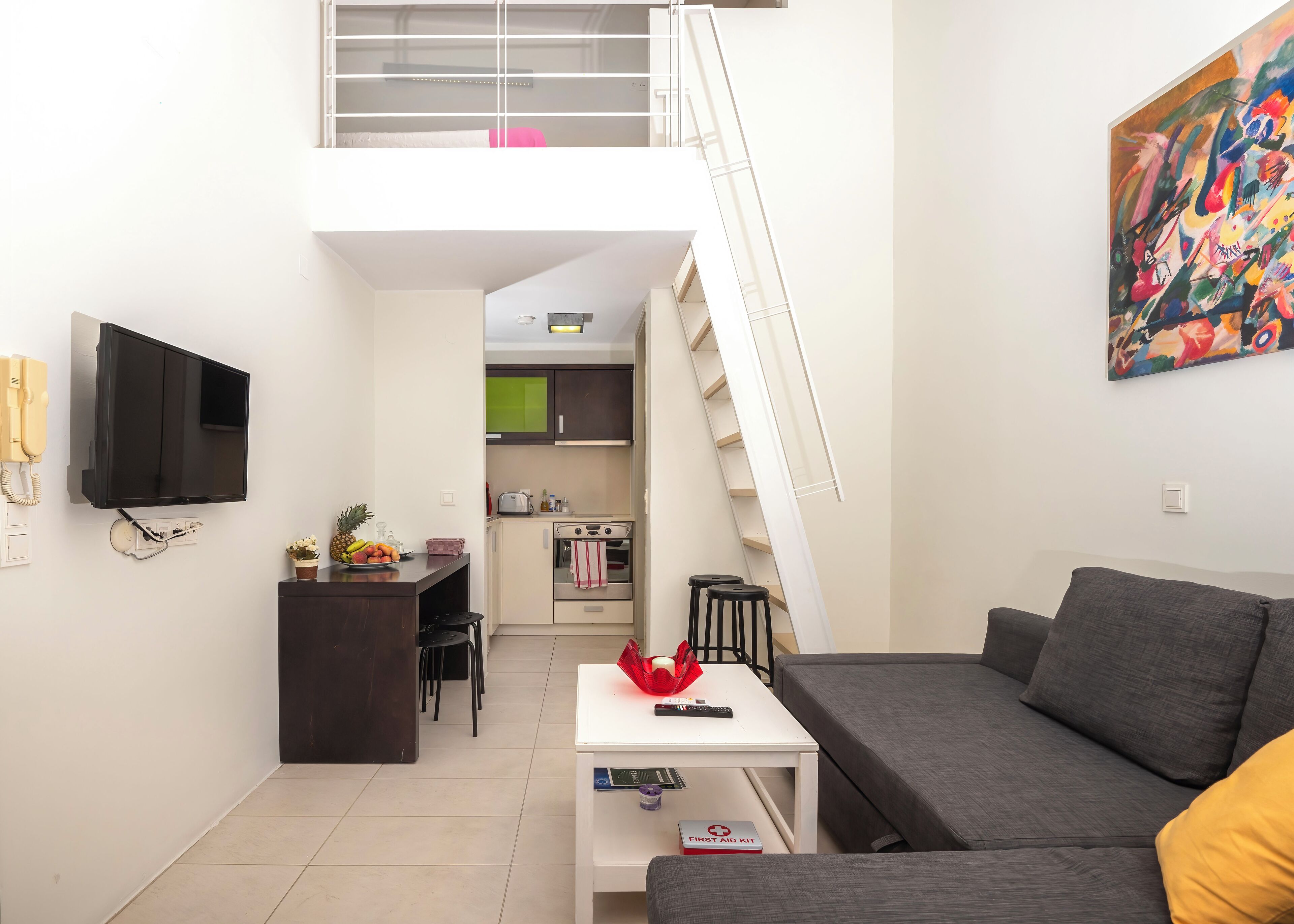 Un espai habitable compacte amb cuineta, zona de menjador, sofà i escala que condueix a una planta superior.