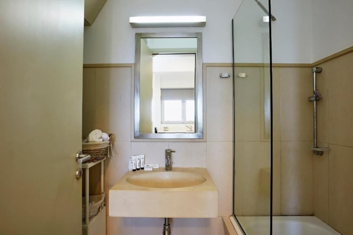 Een badkamer met een wastafel, spiegel, douche en een handdoekrek met handdoeken.