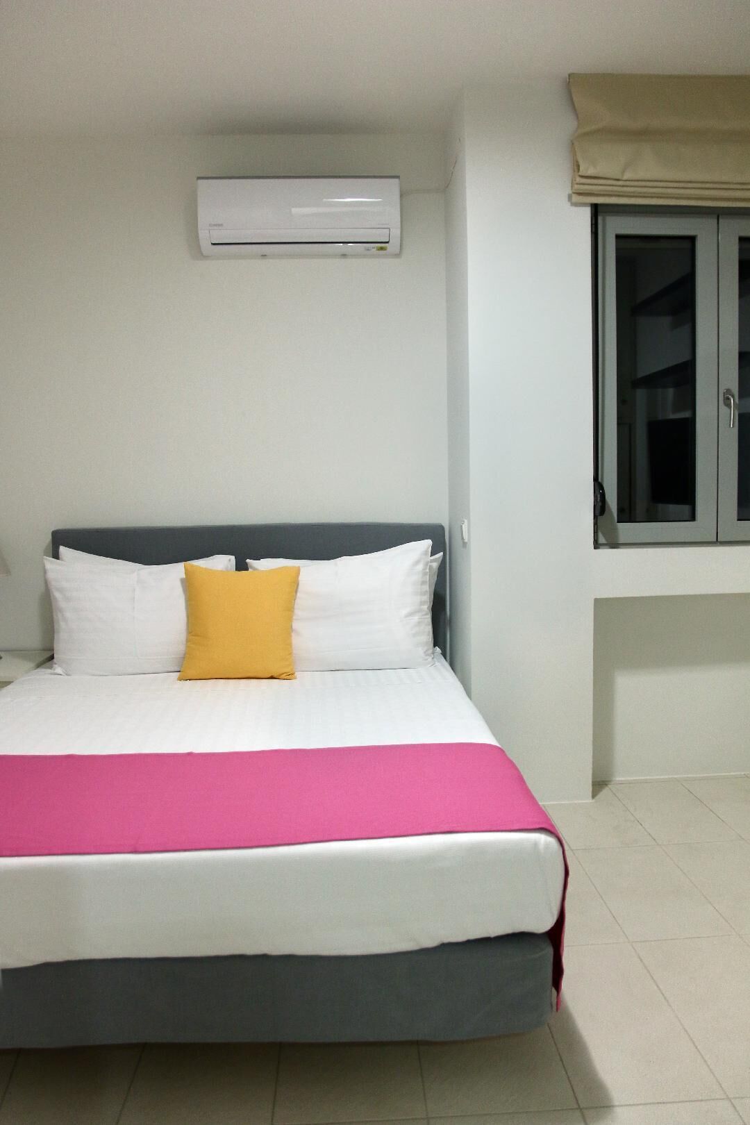 Una cama con ropa de cama blanca y rosa, un cabecero gris y una almohada amarilla.