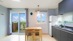 Une cuisine moderne avec une table et des chaises en bois, un réfrigérateur et une vue à travers la porte-fenêtre coulissante.