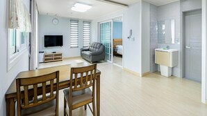 Un salon moderne avec une table à manger et des chaises, un canapé gris, un téléviseur et une grande fenêtre avec des stores.