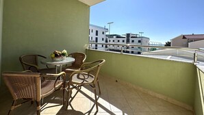 Un balcon avec des fauteuils en osier et une petite table, une plante en pot et une vue sur les immebles.