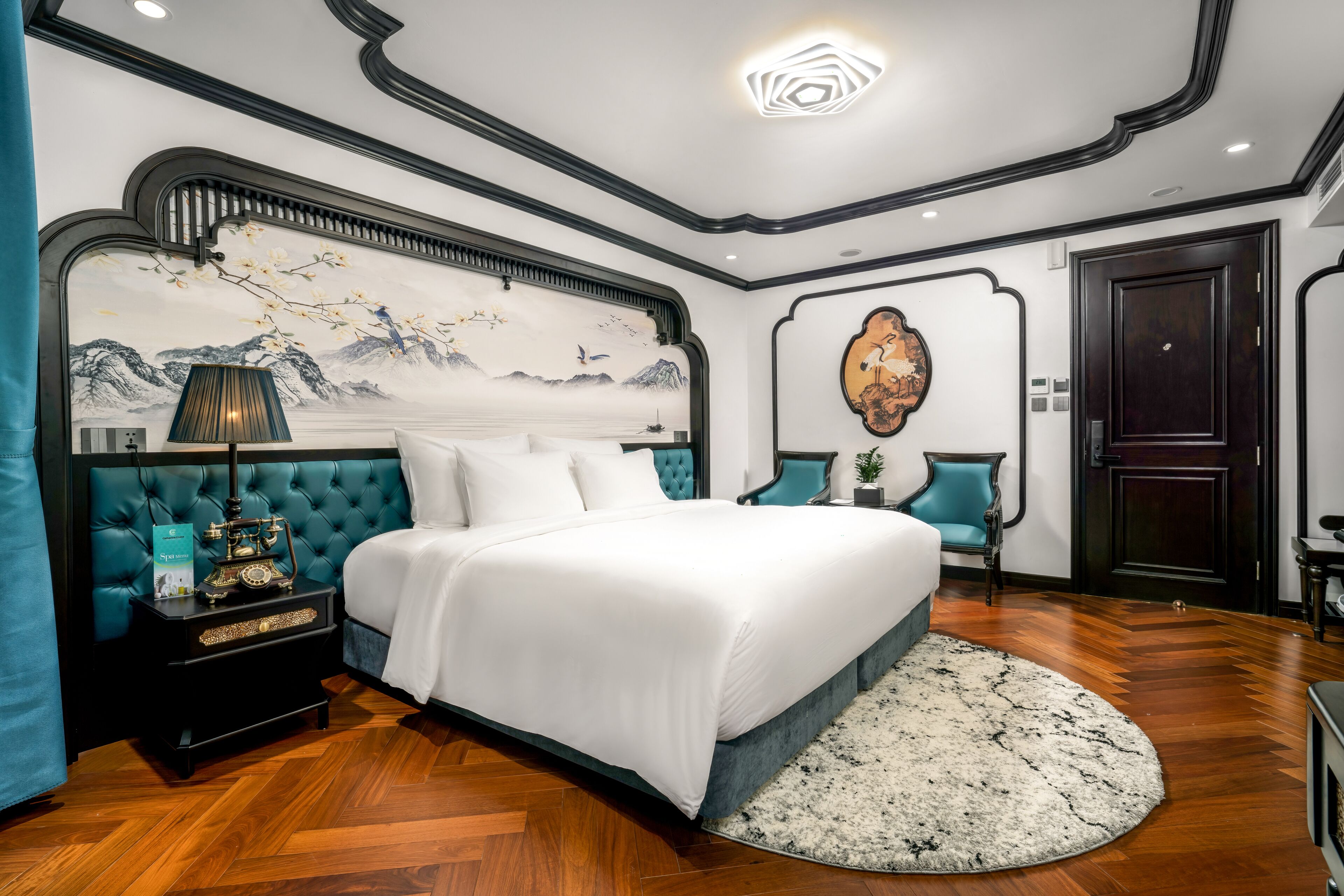A bedroom with a large bed, a nightstand, a wall-mounted lamp, a painting, and a door.