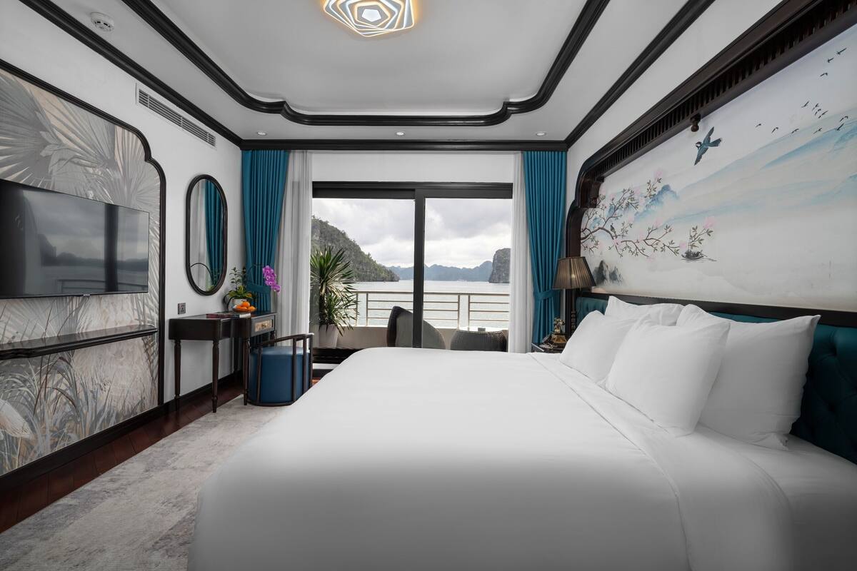 Ein Hotelzimmer mit einem großen Bett, einem Fernseher, einem Gemälde und Blick aufs Meer.