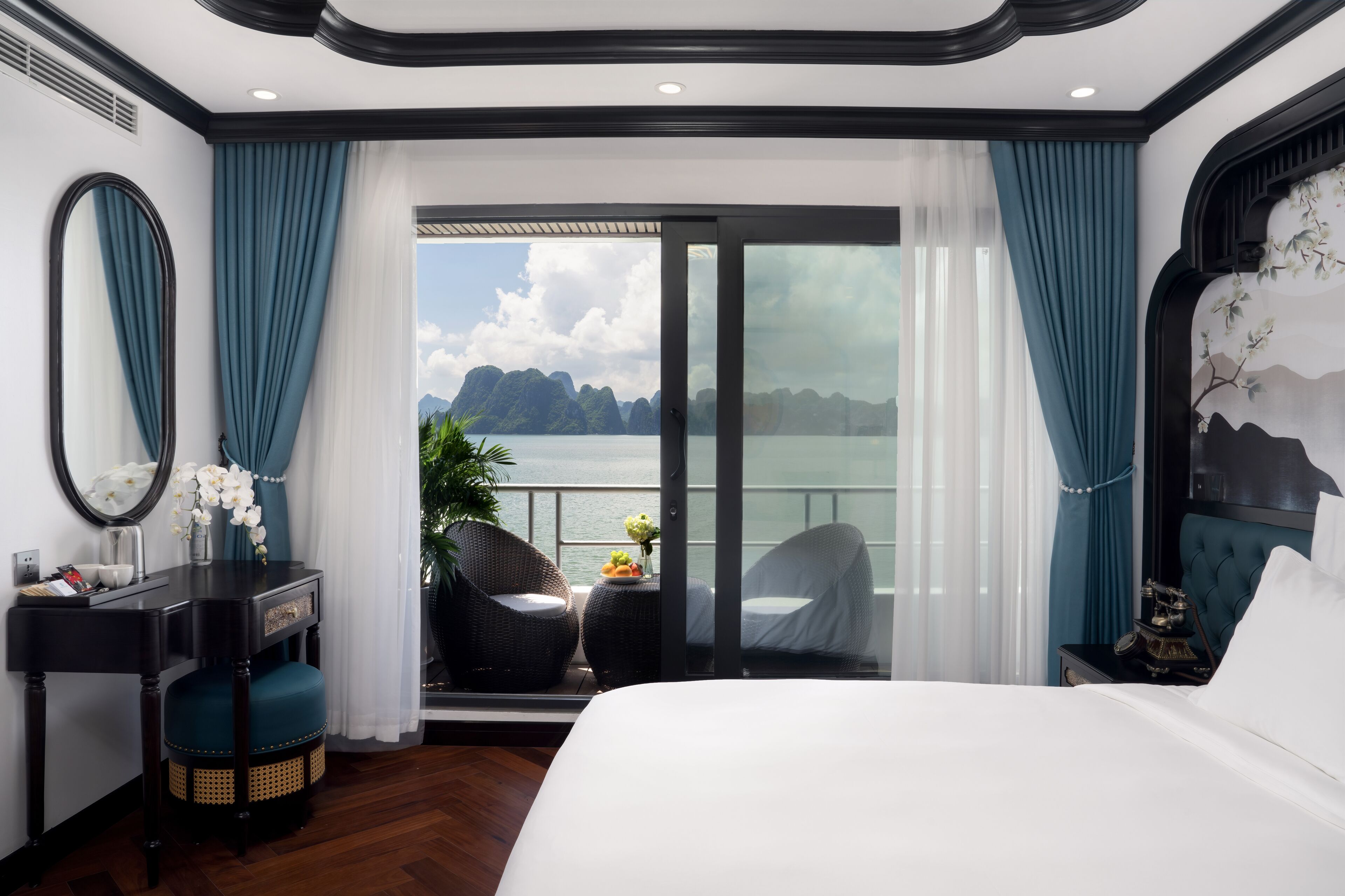 A hotel room with a large bed, a desk with a mirror, and a view of the sea.