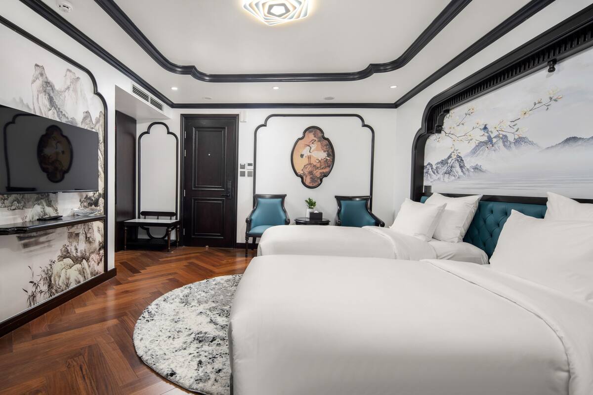 Ein modernes Hotelzimmer mit einem großen Bett, einer Sitzecke mit zwei Sesseln, einem kleinen Tisch und Kunstwerken an den Wänden.