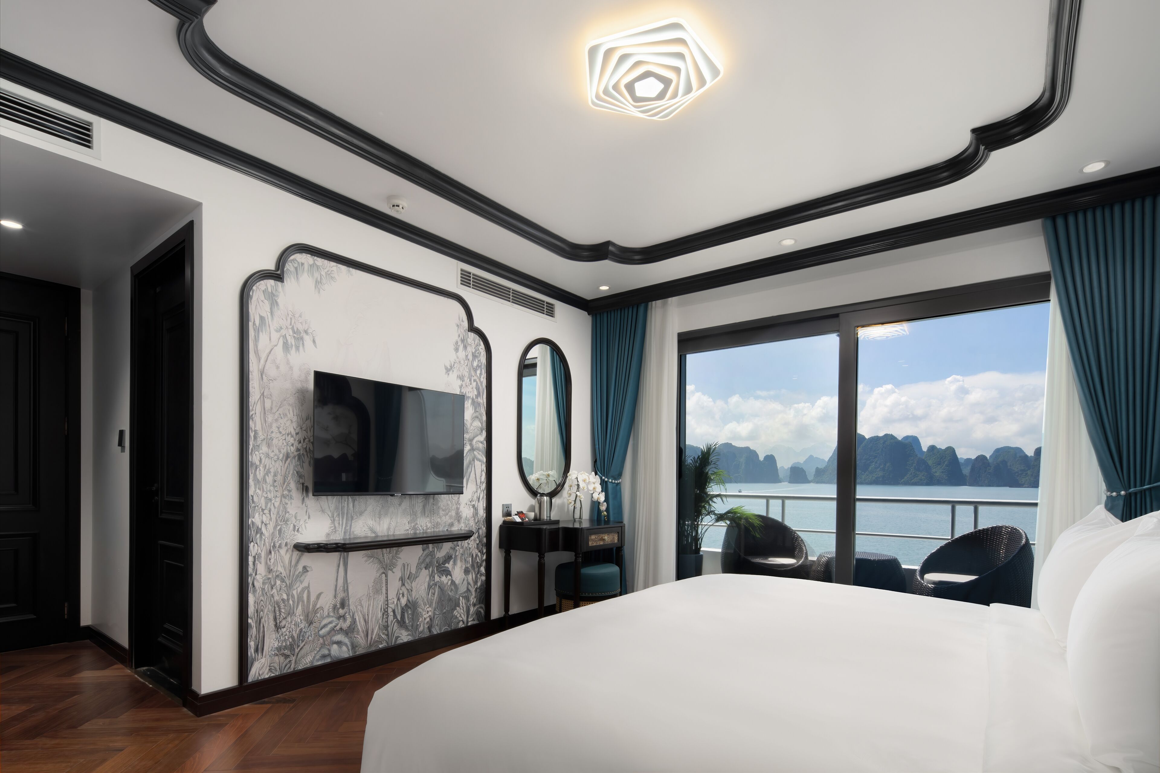 Ein modernes Hotelzimmer mit einem großen Bett, einem Fernseher, einem Schminktisch mit Spiegel und Meerblick.