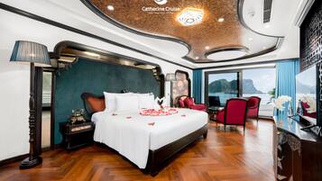 A spacious bedroom with a large bed, a sitting area with a red chair, and a view of the sea.