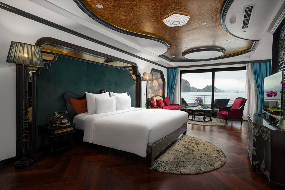 Ein luxuriöses Schlafzimmer mit einem großen Bett, einer klassischen Lampe, einem Schreibtisch und Meerblick.
