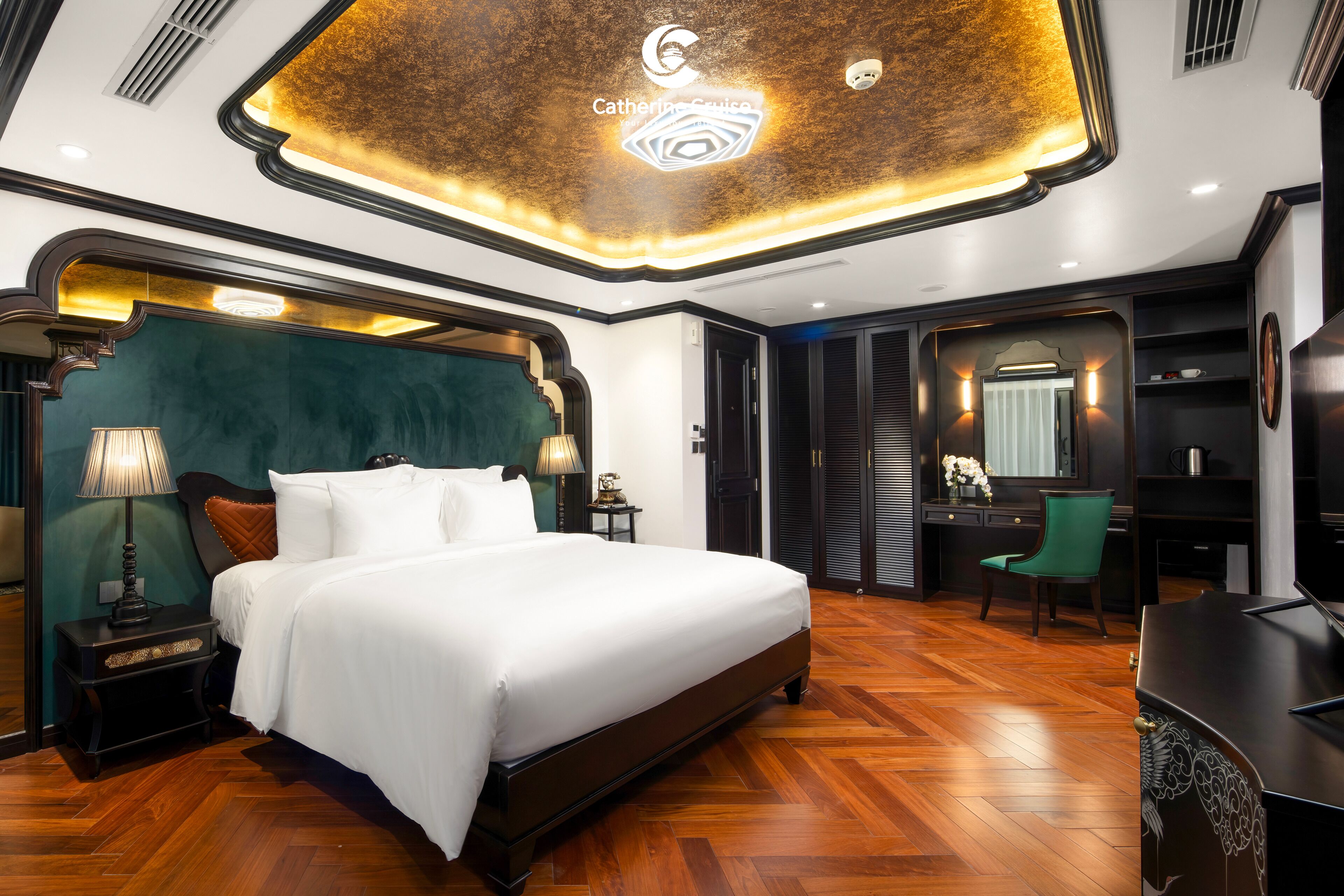 A spacious bedroom with a large bed, a desk, and a chair, featuring a modern ceiling design and wooden flooring.
