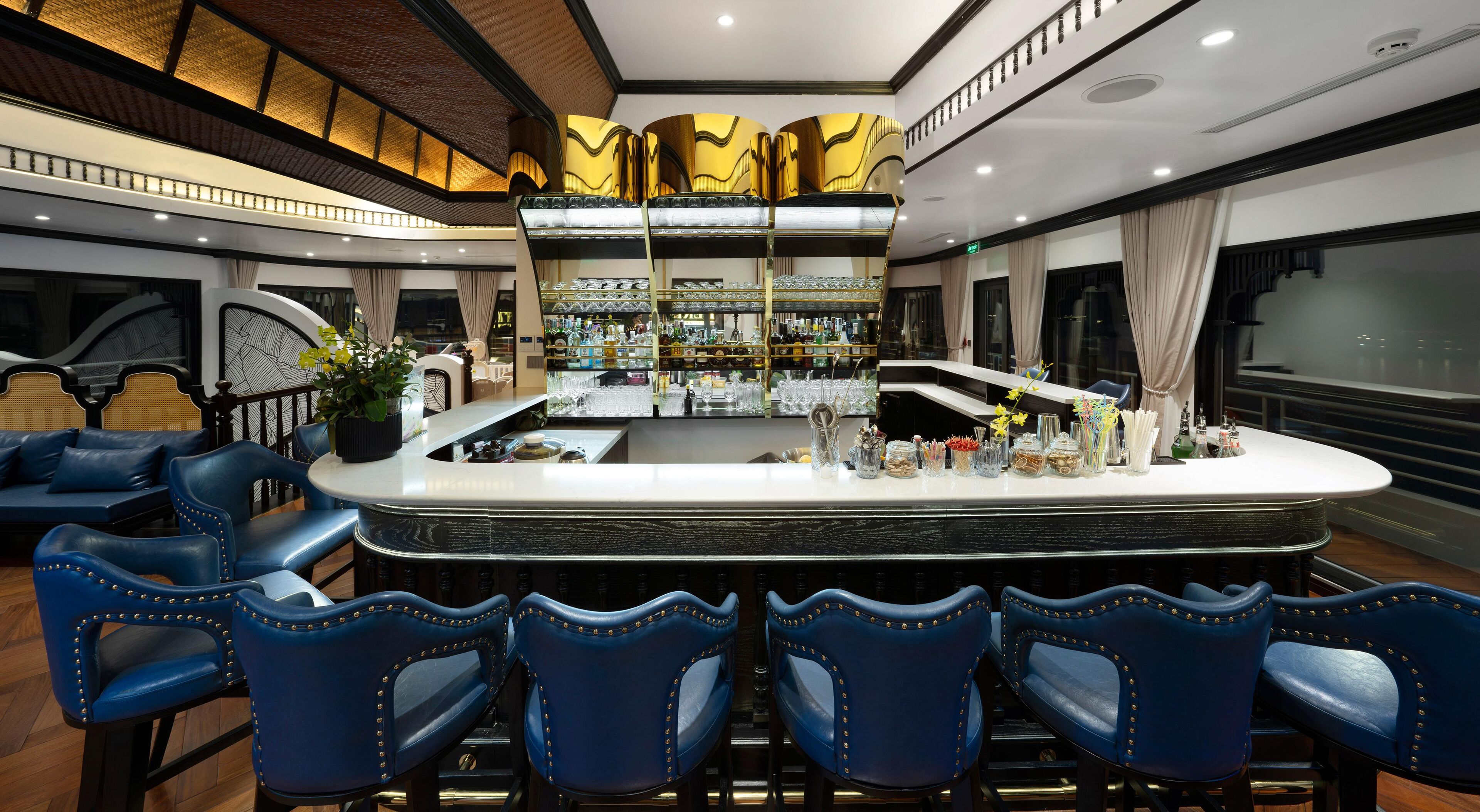 A bar area with a central island, blue upholstered chairs, and a bar counter with various items.
