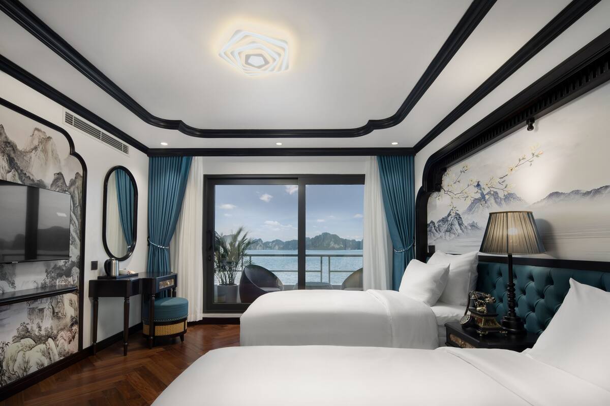 Ein Hotelzimmer mit einem großen Bett, einem Nachttisch mit Lampe, einem Fernseher und Blick aufs Meer.