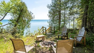 Ein ruhiger Sitzbereich im Freien mit Adirondack-Stühlen und einem Feuerkorb, mit Blick auf einen stillen See und einen dichten Wald.
