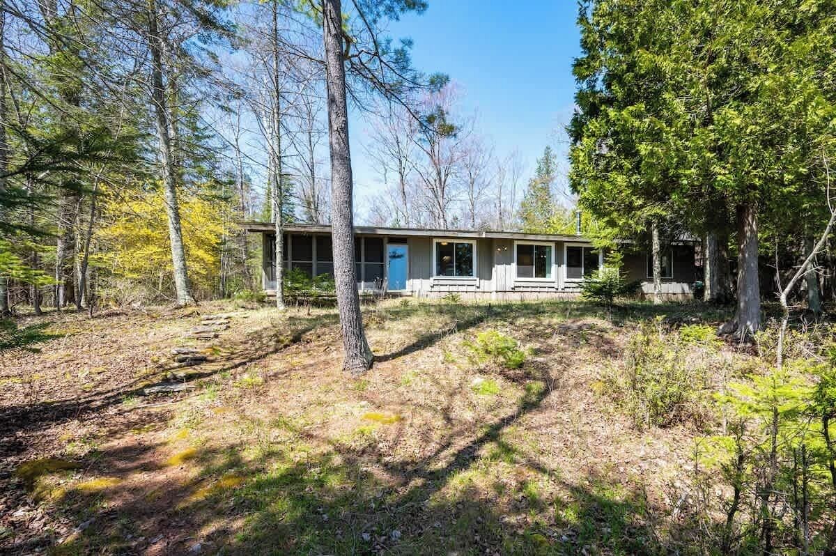A single-story cabin with a front porch, surrounded by trees.