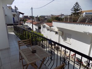 A balcony with a table and chairs, overlooking a residential area with houses and a tree. - Beautiful Modern apt in Skiathos (Skiathos)