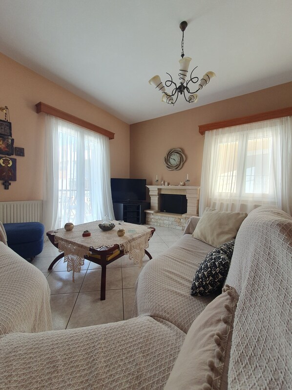 A living room with a fireplace, a dining table, and a blue armchair. - Beautiful Modern apt in Skiathos (Skiathos)