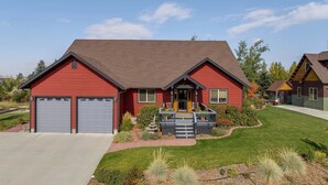 A two-story house with a red exterior, a grey garage, and a front porch with steps leading to the entrance. - Large Teton Family Home w/Hot Tub + Pool Table (Driggs)