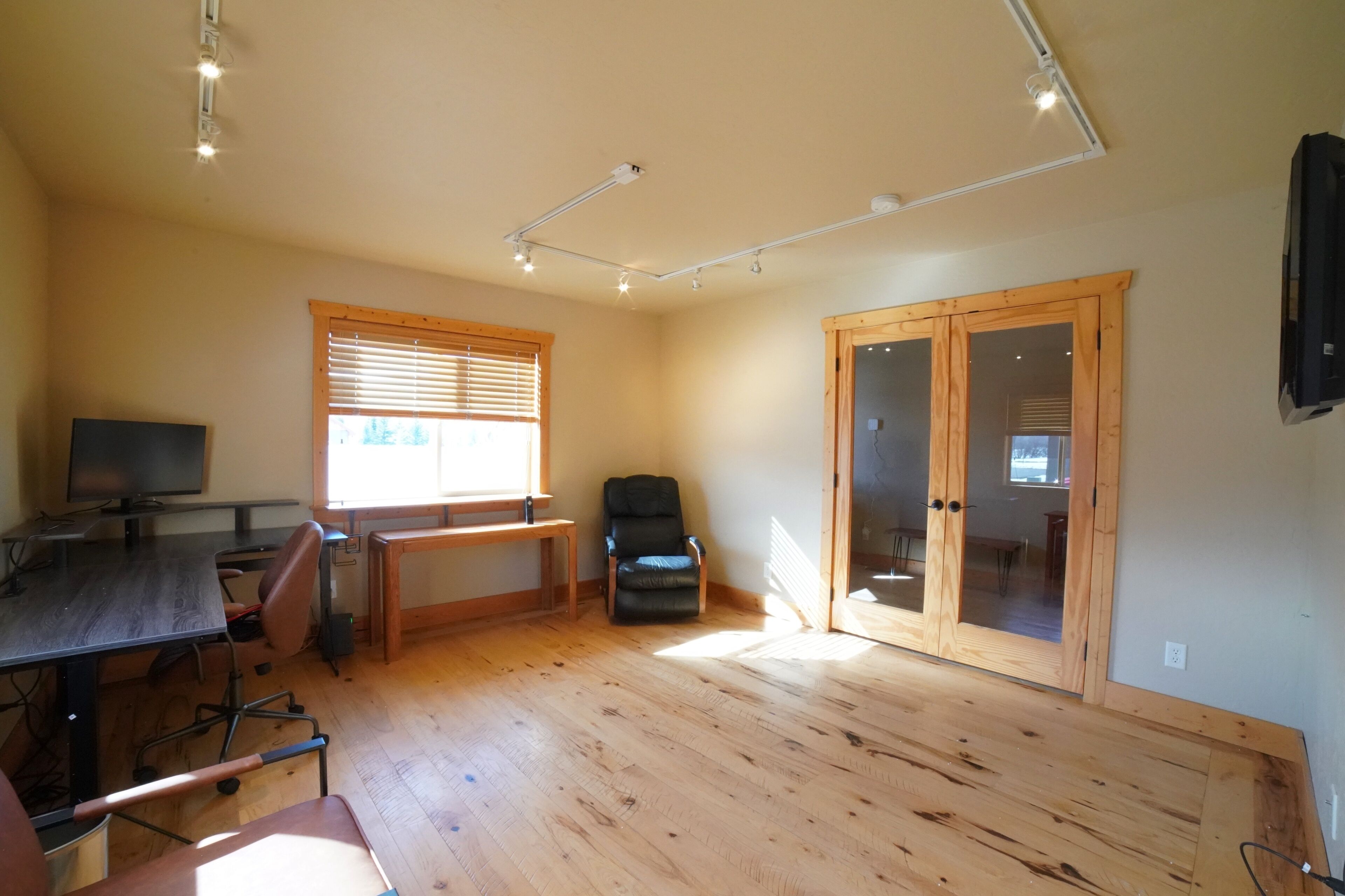 A spacious room with wooden flooring, a desk with a computer, a chair, and a large sliding glass door leading to another room.