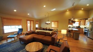 A spacious living room with a sectional sofa, a coffee table, and a dining area with a kitchen in the background. - Large Teton Family Home w/Hot Tub + Pool Table (Driggs)