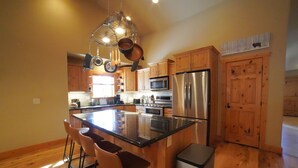 A modern kitchen with wooden cabinets, stainless steel appliances, and a central island with bar stools. - Large Teton Family Home w/Hot Tub + Pool Table (Driggs)