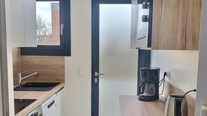 A compact kitchen with white cabinets, a black door, and a window.