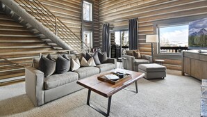 A log cabin interior with a sofa, ottoman, coffee table, and a staircase.