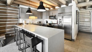 A modern kitchen with a large island, stainless steel appliances, and a rustic wooden ceiling.