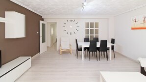 Moderni ruokailutila, jossa on valkoinen pöytä ja tuolit, suuri seinäkello ja geometrisesti kuvioitu katto.