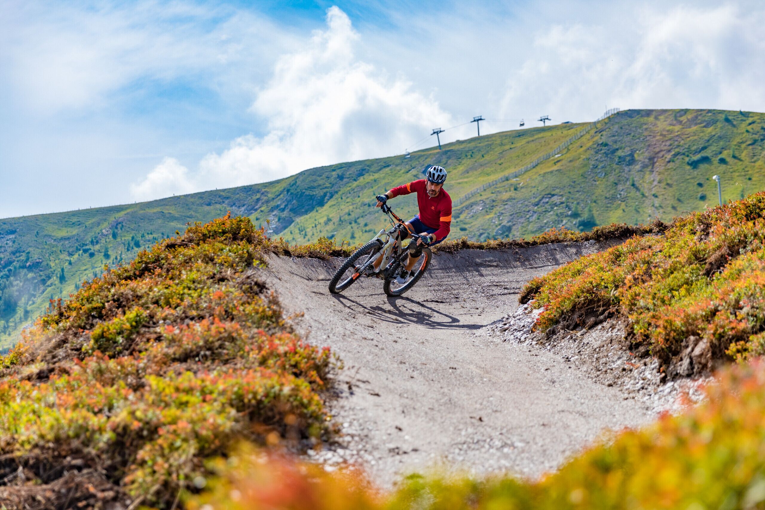 Een mountainbiker op een onverharde pad met een heuvelachtig landschap en elektriciteitslijnen op de achtergrond.